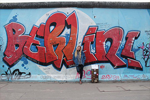 Student standing in front of the Berlin Wall covered in street art