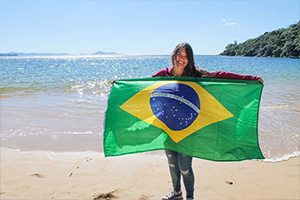 Student on beach holding Brazilian flag