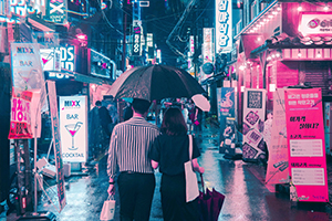 Couple walking down a bustling city street at night in the rain