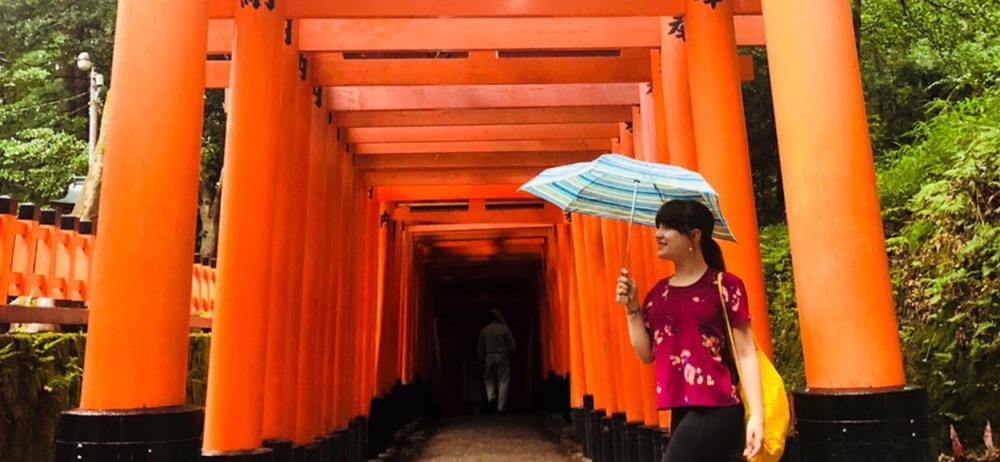 Student walking by Tori Shrines in Japan with umbrella