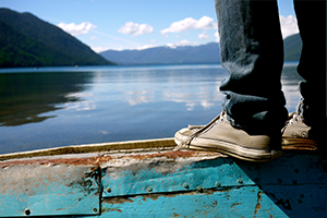 Person in converse sneakers standing on the edge of a boat overlooking Chilean lake with mountains